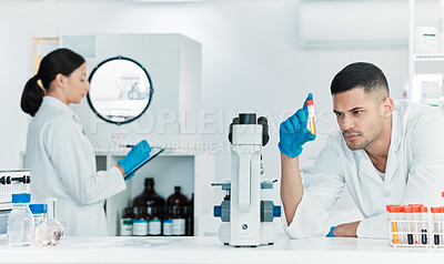 Buy stock photo Shot of a young scientist analysing samples while working in a lab with a colleague in the background