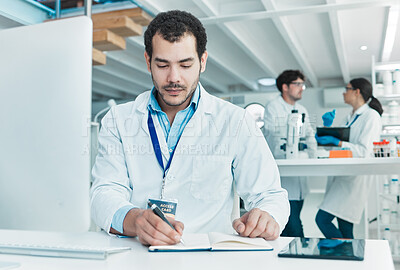 Buy stock photo Shot of a young scientist writing notes while working on a computer in a lab