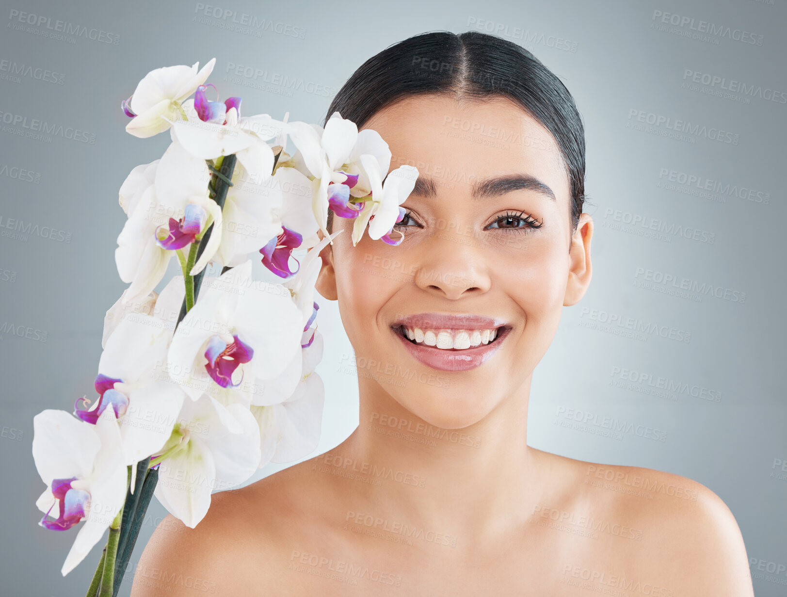 Buy stock photo Portrait, beauty or girl with flowers for skincare or cosmetology for natural shine on grey background. Floral cosmetics, moth orchids and happy woman with healthy glow, smile or results in studio