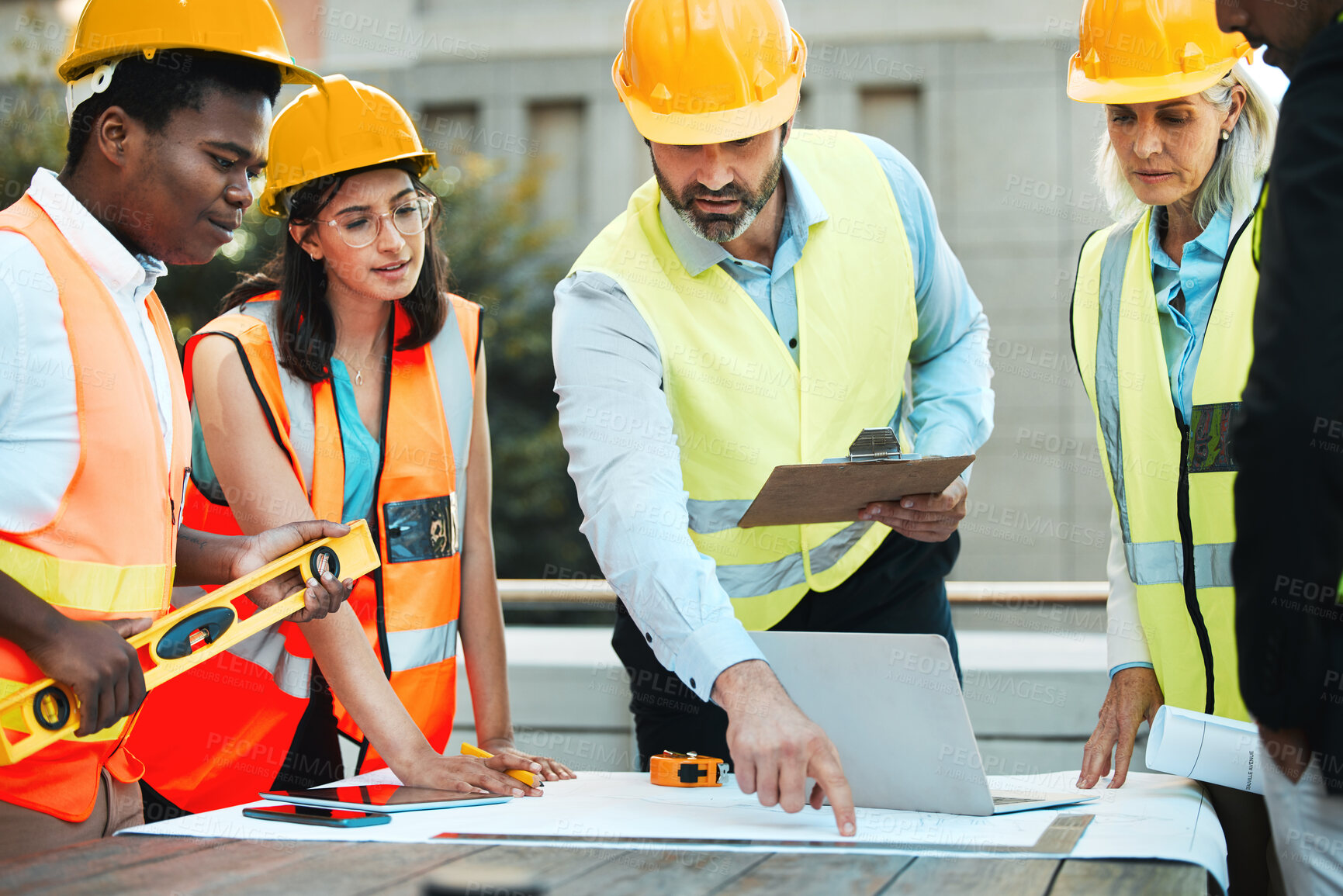 Buy stock photo Shot of a diverse group of contractors standing outside together and having a discussion over building plans