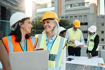 Buy stock photo Shot of two contractors standing outside together and using a laptop while their colleagues work behind them