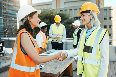 Buy stock photo Shot of two contractors standing outside together and shaking hands while their colleagues work behind them
