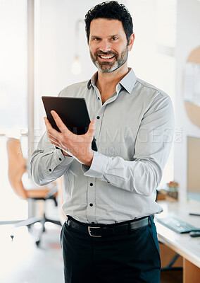Buy stock photo Shot of a mature businessman standing alone in the office and using a digital tablet