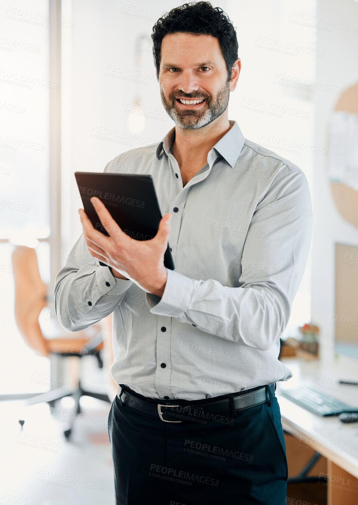 Buy stock photo Shot of a mature businessman standing alone in the office and using a digital tablet