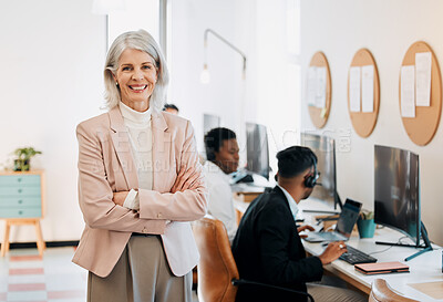 Buy stock photo Shot of a mature businesswoman standing in the office with her arms folded while her team work behind her