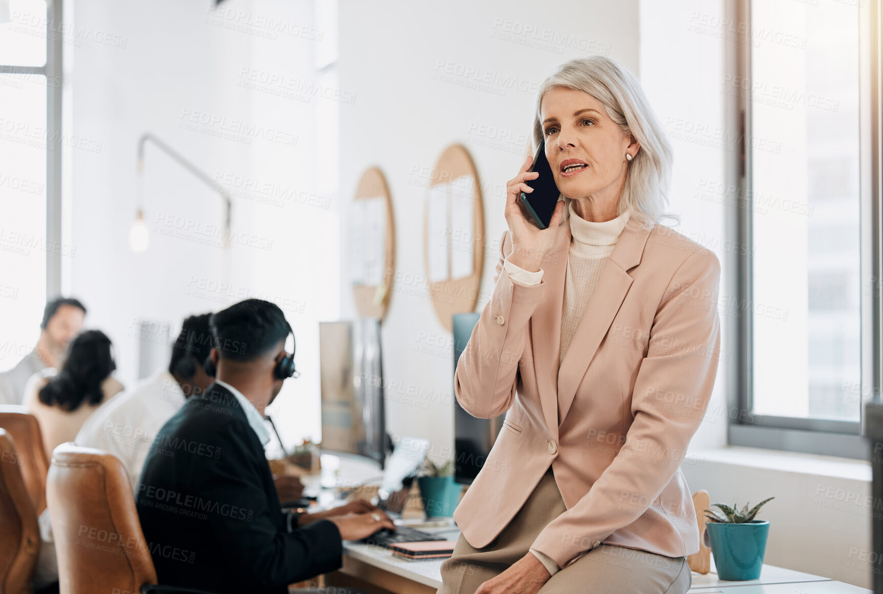 Buy stock photo Mature woman, phone call and talk in contact center in office with team, listen and leader with customer service. Person, crm and smartphone for tech support, job or help desk at telemarketing agency