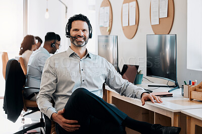 Buy stock photo Shot of a mature businessman sitting in the office and wearing a headset while his colleagues work behind him