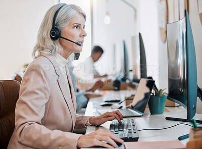 Buy stock photo Shot of a mature agent sitting in the office and using her computer while her colleagues work behind her