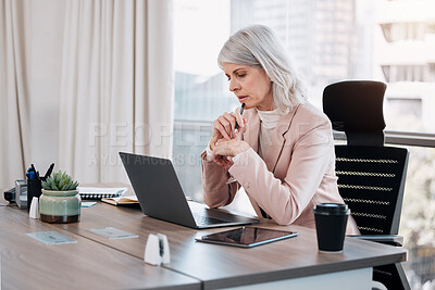 Buy stock photo Shot of a mature businesswoman sitting alone in the office and looking contemplative while using her laptop