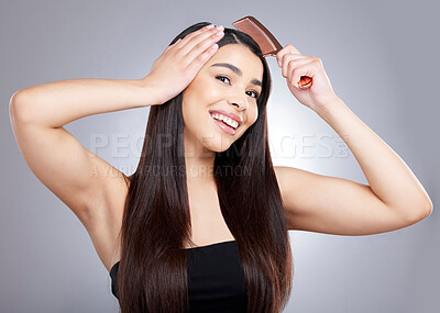 Buy stock photo Studio portrait of an attractive young woman combing her hair against a grey background