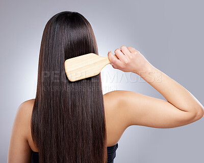 Buy stock photo Rearview shot of a young woman combing her hair against a grey background