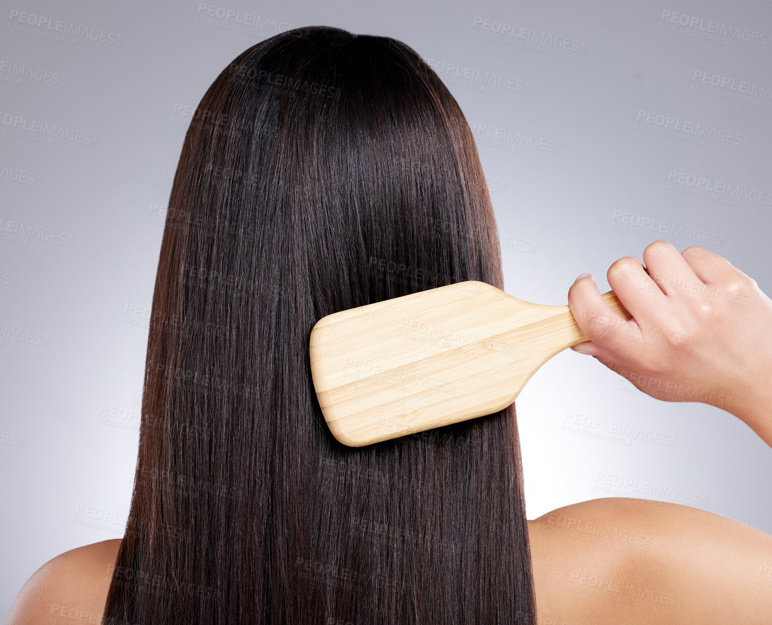 Buy stock photo Rearview shot of a young woman combing her hair against a grey background