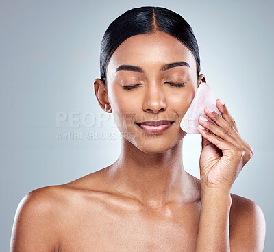 Buy stock photo Beauty, skincare and gua sha with face of woman in studio for massage, wellness and cosmetics. Spa, self care and glow with model on grey background for facial, cosmetology and rose quartz crystal