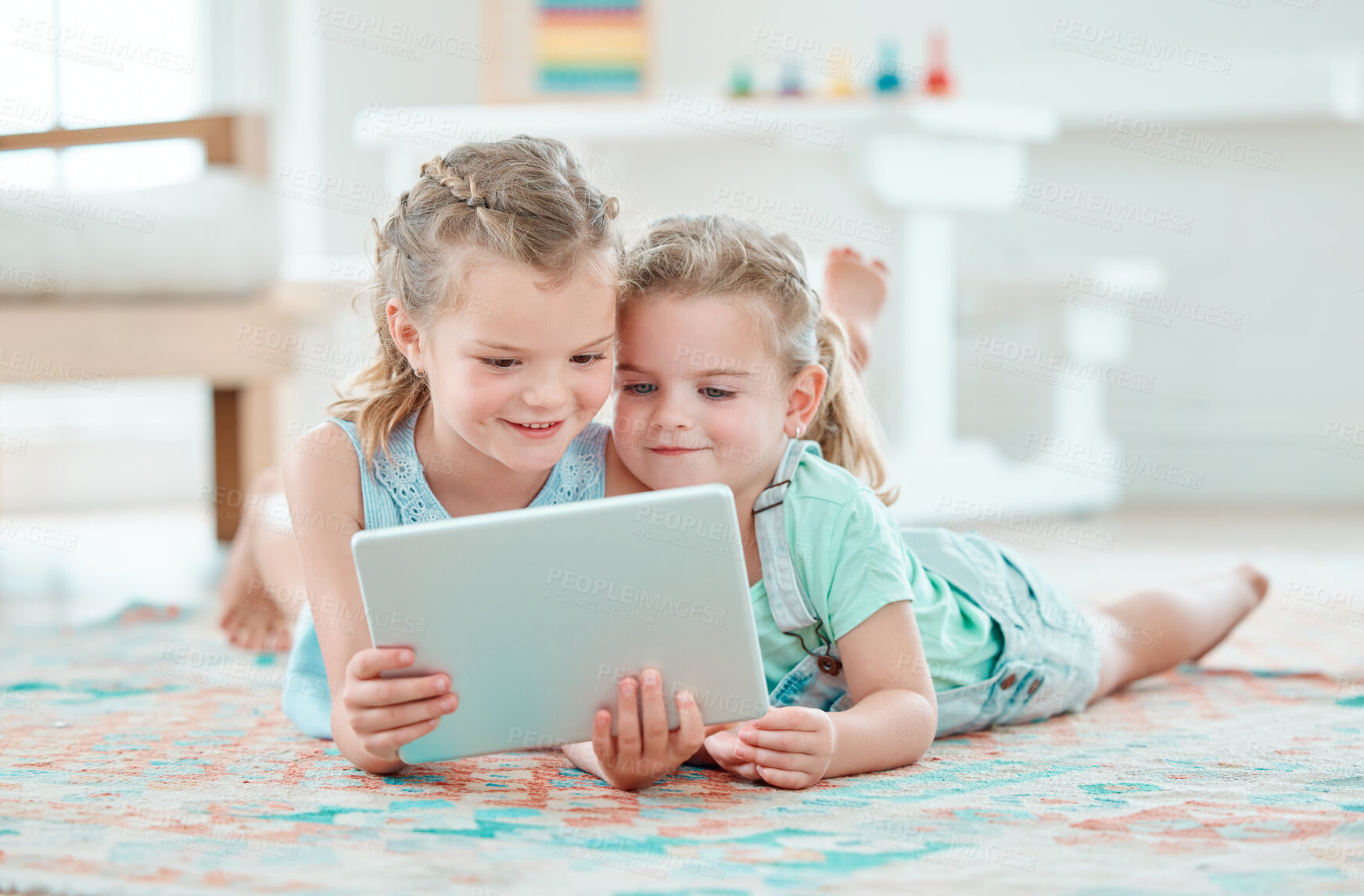 Buy stock photo Shot of two adorable girls using a digital tablet while lying on the floor at home
