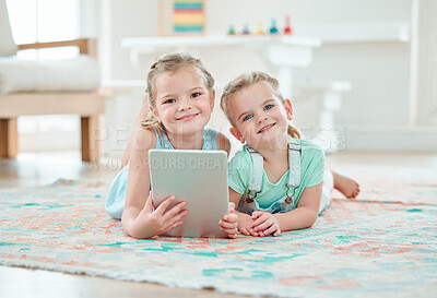 Buy stock photo Shot of two adorable girls using a digital tablet while lying on the floor at home