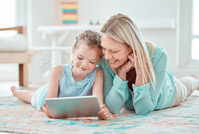 Buy stock photo Shot of an adorable little girl using a digital tablet while lying at home with her mother