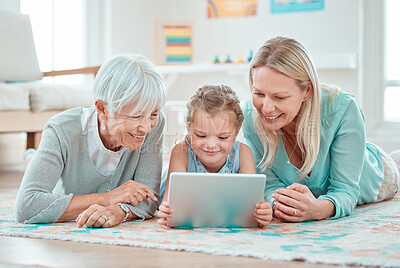 Buy stock photo Shot of an adorable little girl using a digital tablet while lying at home with her mother and grandmother