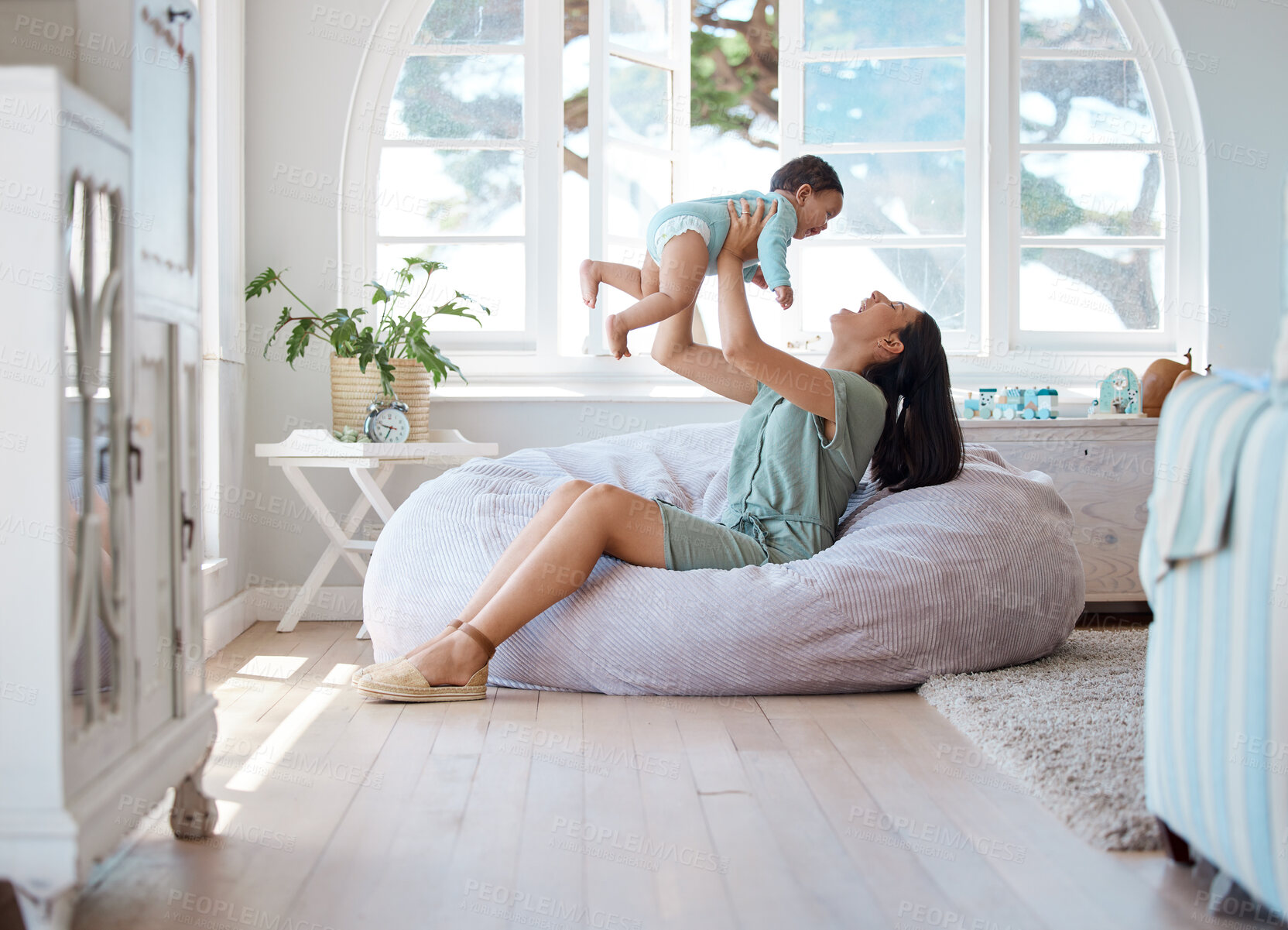 Buy stock photo Happy mom, play and holding baby in air at home for love, care and quality time together for childhood happiness. Mother, infant and carrying newborn kid on bean bag in living room for laughing fun