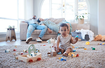 Buy stock photo Shot of a little girl playing on the floor while her parents nap in the background