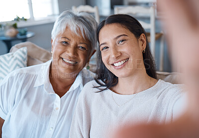 Buy stock photo Shot of a young woman taking a selfie while bonding with her mother on a sofa at home
