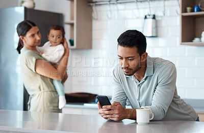 Buy stock photo Shot of a young man ignoring his wife and child while using his phone at home