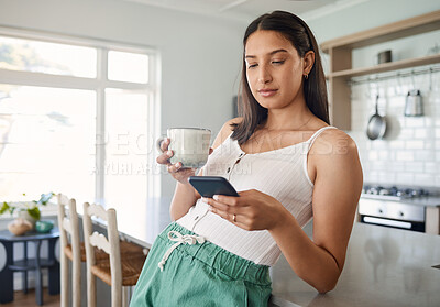 Buy stock photo Shot of a woman holding her cellphone while drinking coffee at home