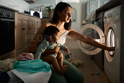 Buy stock photo Shot of a mom doing laundry at night with her baby on her arm