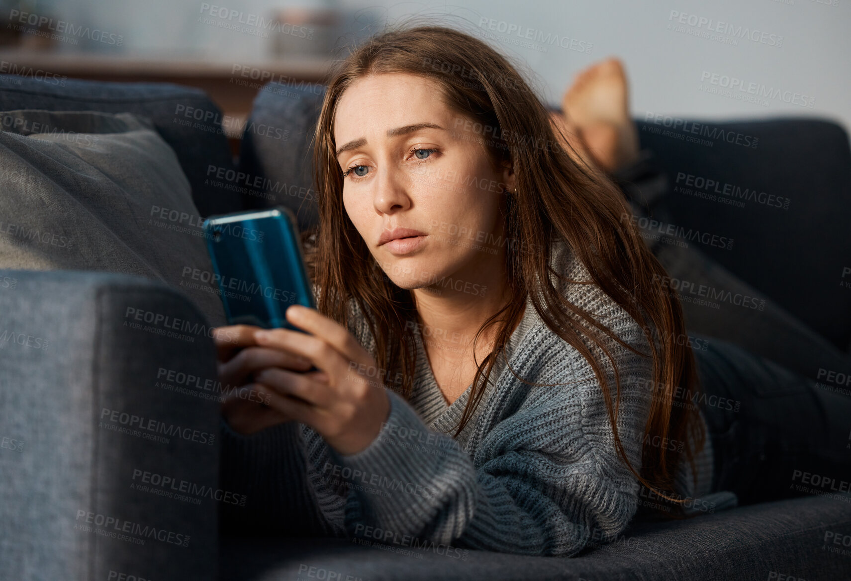 Buy stock photo Shot of a young woman looking depressed while using her smartphone