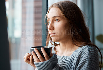 Buy stock photo Shot of a unhappy young woman drinking tea while looking out of the window