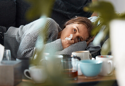 Buy stock photo Shot of a young woman lying on her couch blowing her nose and looking depressed