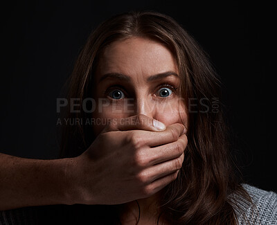 Buy stock photo Shot of a scared young woman’s mouth being covered by an unrecognisable man’s hand against a black background