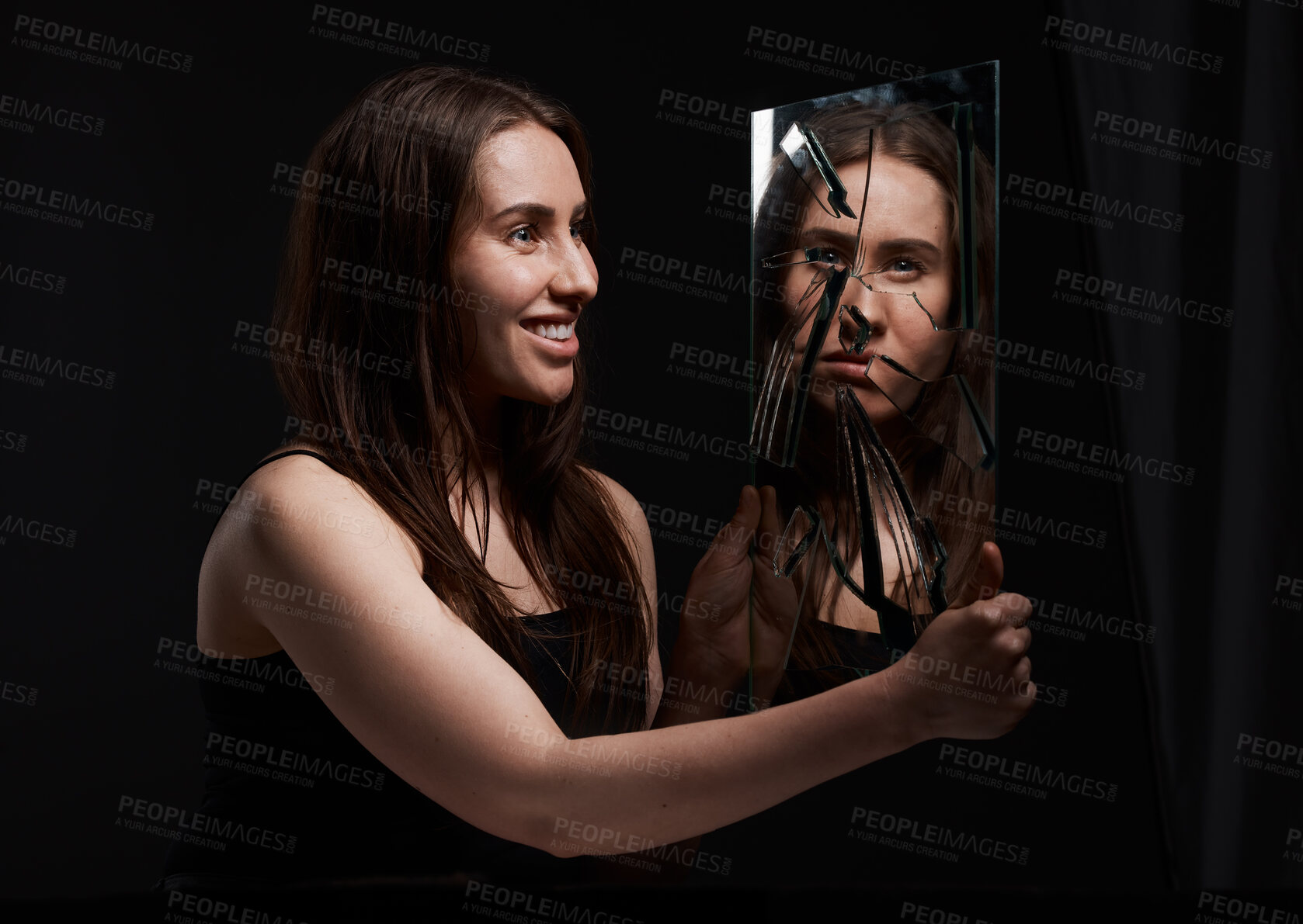 Buy stock photo Shot of a creepy woman grinning at her reflection in a broken mirror