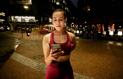 Buy stock photo Shot of a young woman using a phone while on a run at night