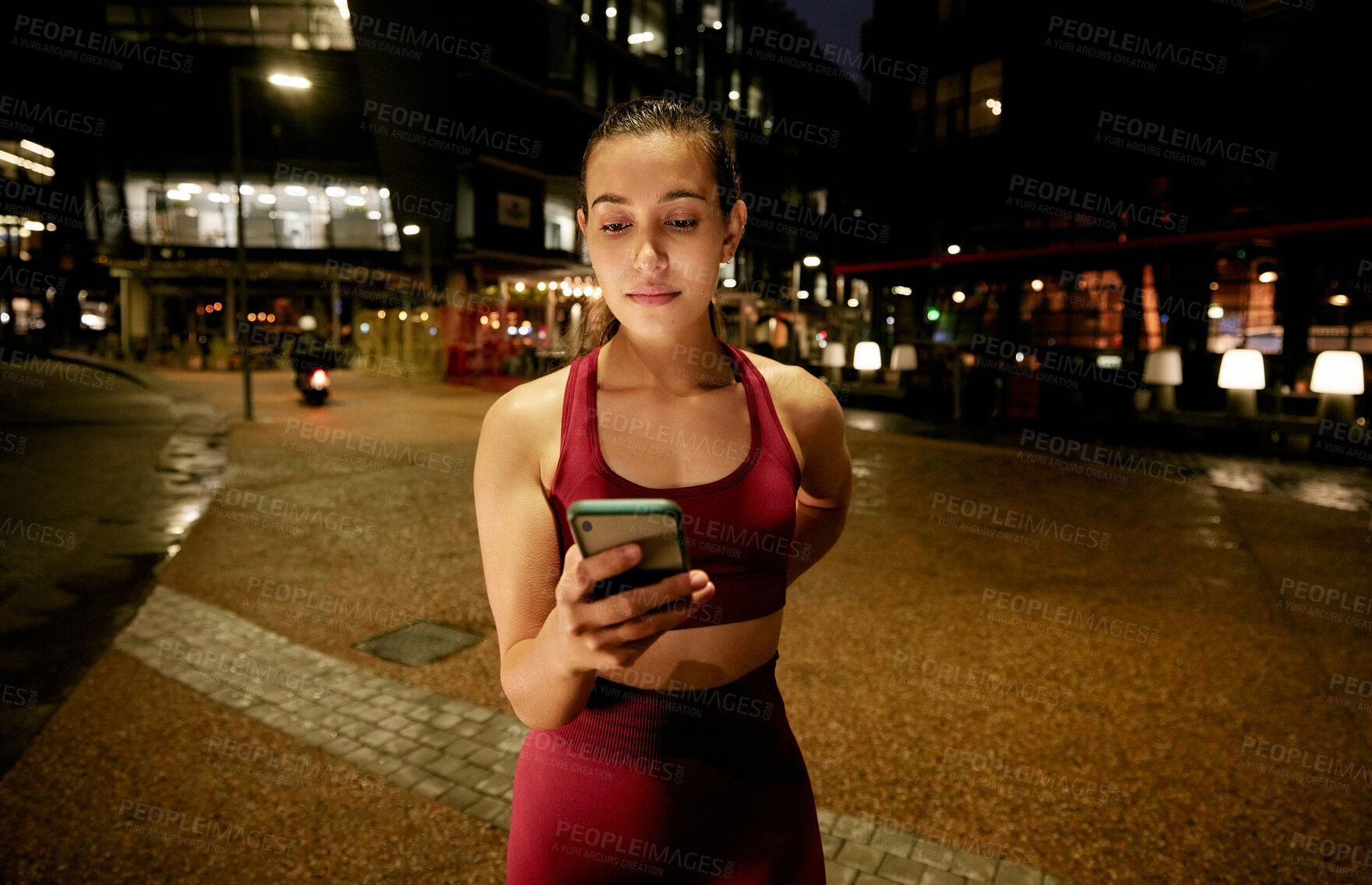 Buy stock photo Shot of a young woman using a phone while on a run at night