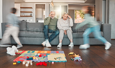 Buy stock photo Shot of two grandparents looking tired while their grandchildren run around at home