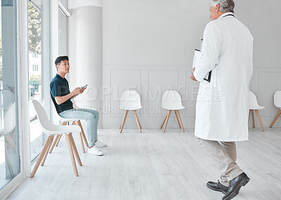 Buy stock photo Shot of a young man using a cellphone while sitting in the waiting room of a clinic