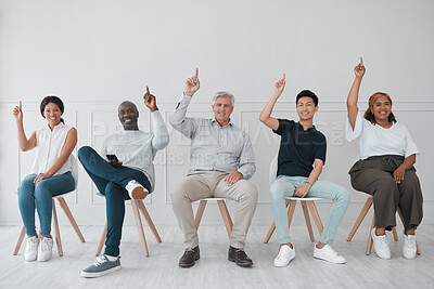 Buy stock photo Portrait of a diverse group of people pointing up while sitting in line against a white background