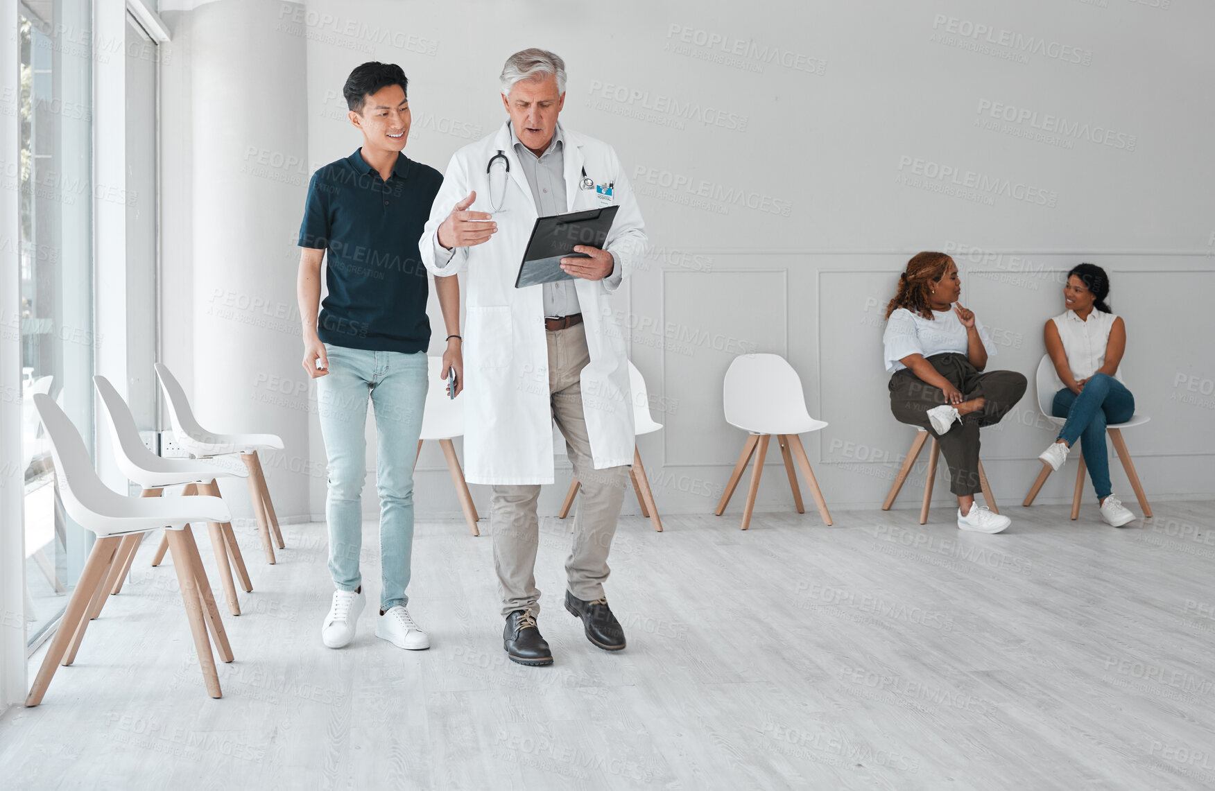Buy stock photo Shot of a mature doctor meeting with a young man in the waiting room of a clinic