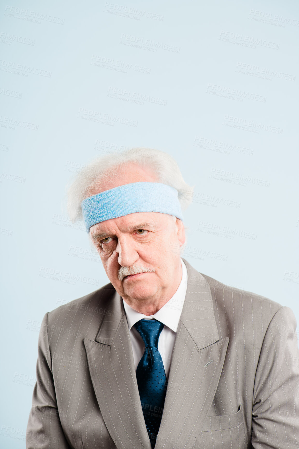 Buy stock photo Shot of a senior man sitting alone in the studio and looking grumpy while wearing a headband