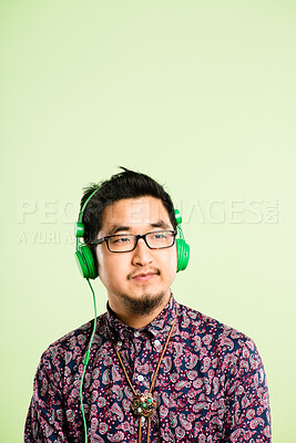 Buy stock photo Headphones, music and Asian man in studio listening to audio, streaming radio and podcast. Mockup, subscription and face of person with earphones for entertainment, relax or chill on green background