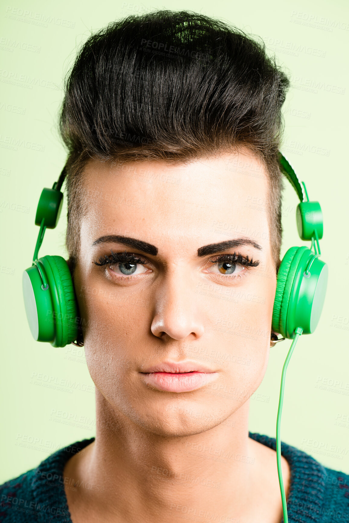 Buy stock photo Headphones, cosmetics and portrait of man in studio listen to audio, streaming radio and podcast. Mockup, fashion and face of person with makeup and entertainment, relax or chill on green background