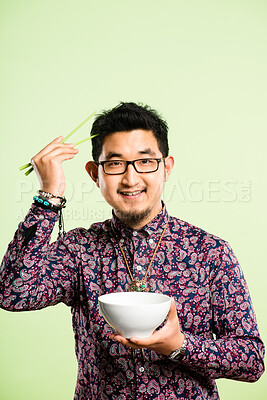Buy stock photo Shot of a handsome young man sitting alone in the studio and eating with chopsticks