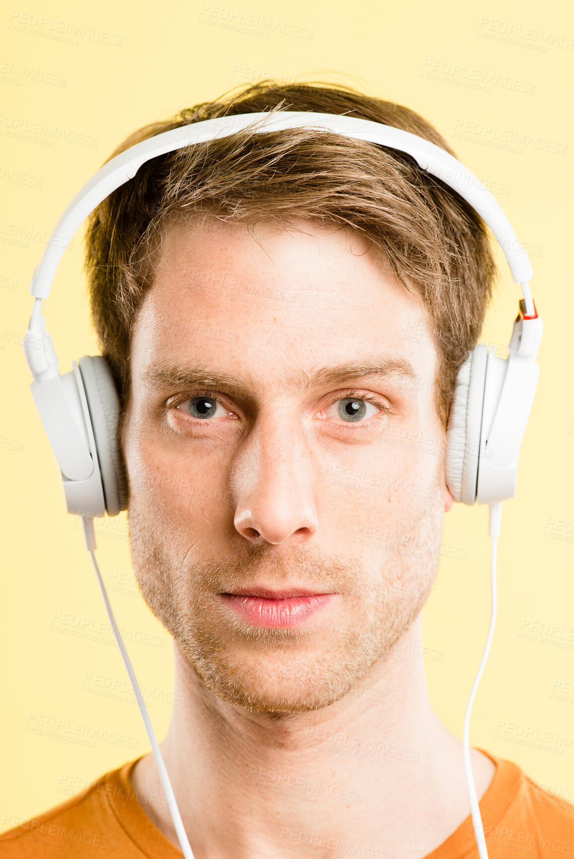 Buy stock photo Shot of a handsome young man standing alone in the studio and listening to music through headphones