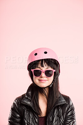 Buy stock photo Shot of an attractive young woman standing alone in the studio and posing while wearing a helmet and sunglasses