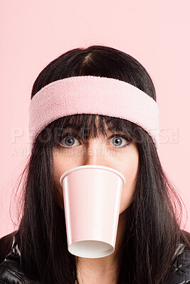 Buy stock photo Shot of a young woman standing in the studio and posing while wearing a headband while biting a coffee cup