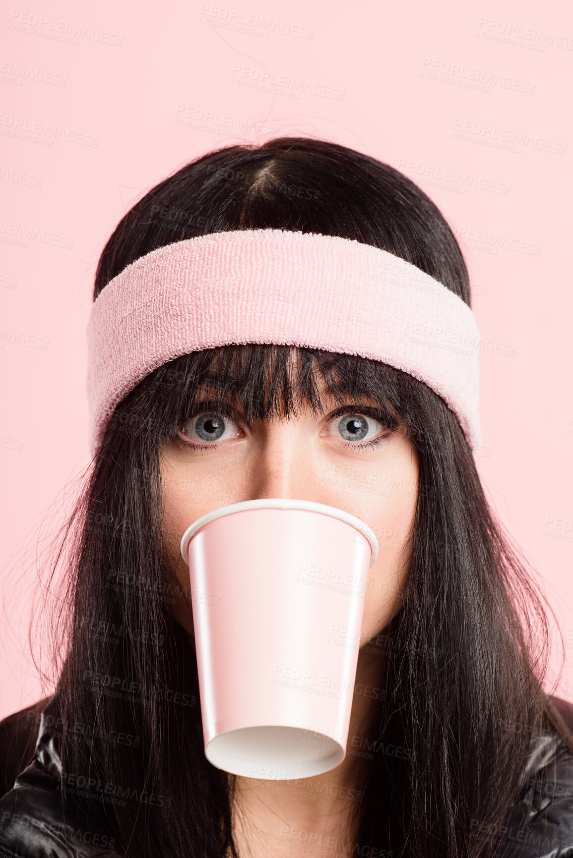 Buy stock photo Shot of a young woman standing in the studio and posing while wearing a headband while biting a coffee cup