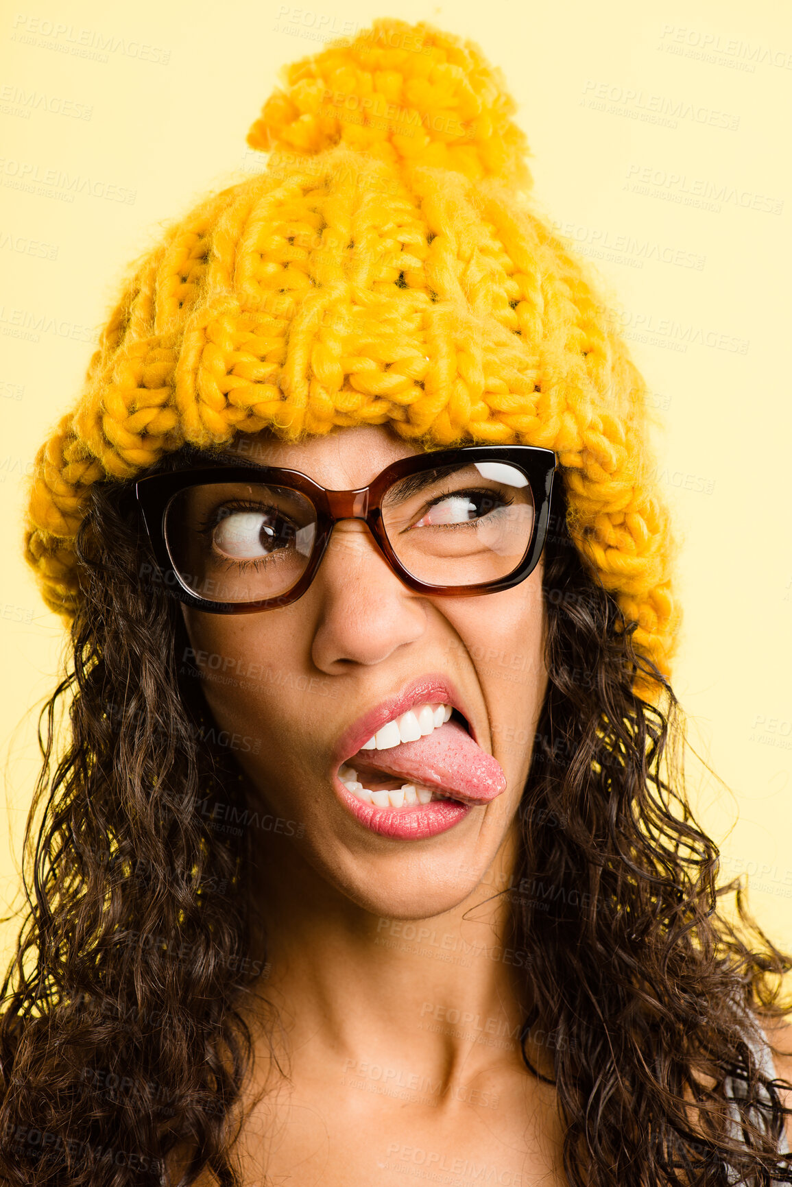 Buy stock photo Shot of an attractive young woman standing alone in the studio and pulling funny faces while wearing a beanie