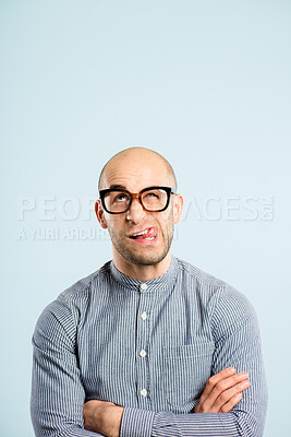 Buy stock photo Shot of a handsome young man sitting alone in the studio with his arms folded and pulling funny faces