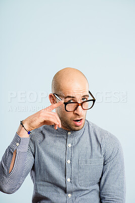 Buy stock photo Shot of a handsome young man sitting alone in the studio and pulling funny faces while wearing glasses