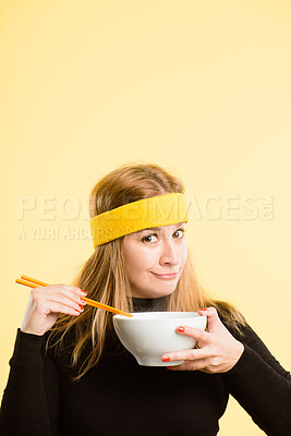 Buy stock photo Shot of an attractive young woman standing alone in the studio and eating with chopsticks